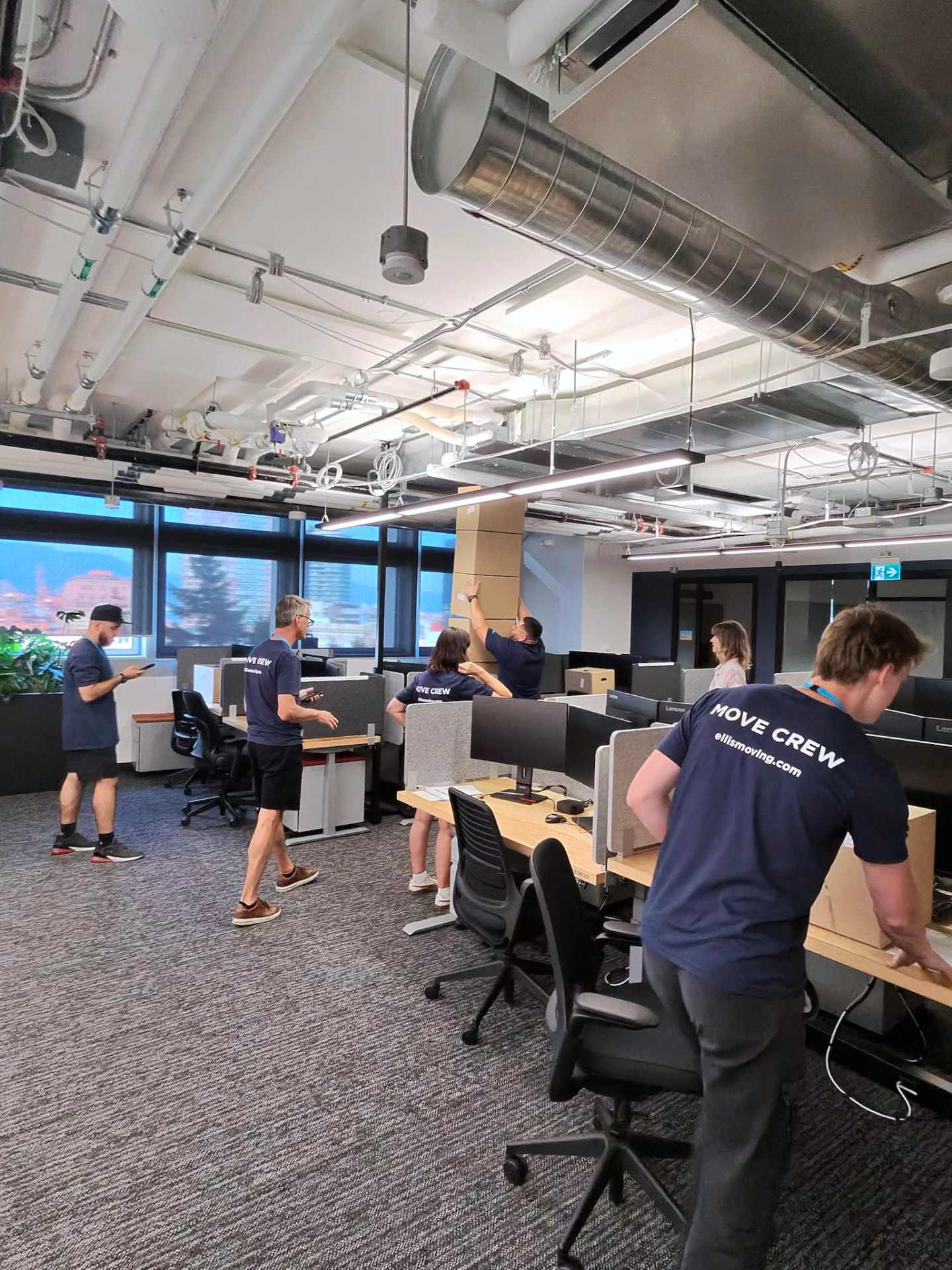 Movers relocating an office with crates and dollies in a mountain-view workspace